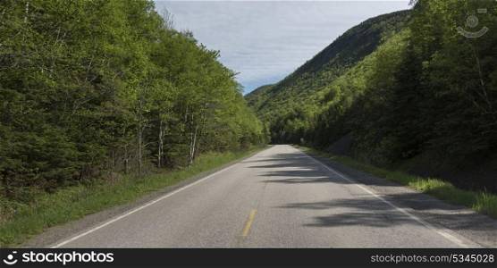 Empty road amidst trees by hills, Petit Etang, Cape Breton Highlands National Park, Cape Breton Island, Nova Scotia, Canada