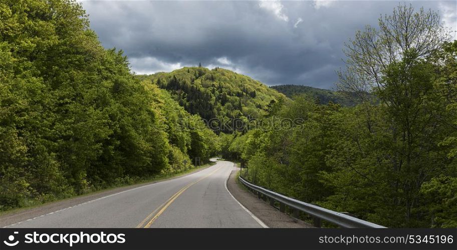 Empty road amidst trees by hills, Pleasant Bay, Cape Breton Highlands National Park, Cape Breton Island, Nova Scotia, Canada