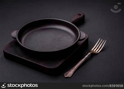 Empty round cast iron skillet on dark textured concrete background. Cutlery, preparation for dinner