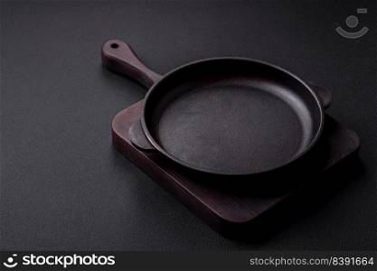 Empty round cast iron skillet on dark textured concrete background. Cutlery, preparation for dinner