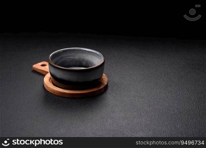 Empty round ceramic bowl on a wooden cutting board in brown color on a dark textured concrete background
