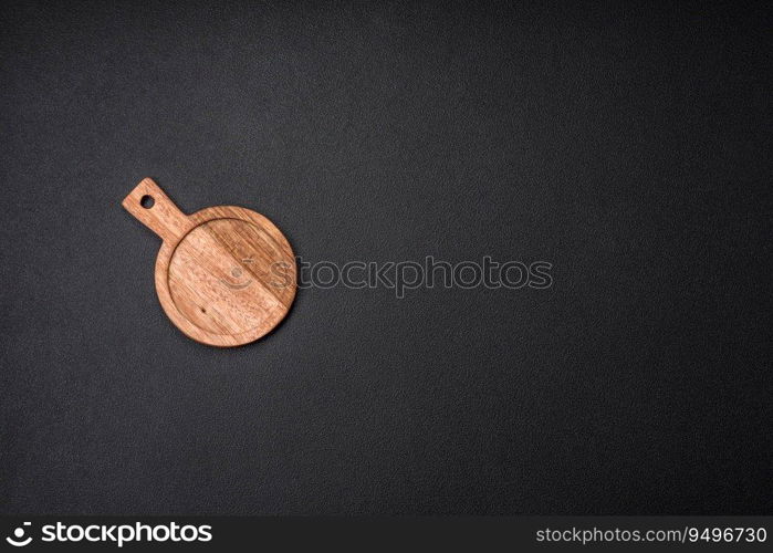 Empty round kitchen wooden cutting board in brown color on a dark textured concrete background