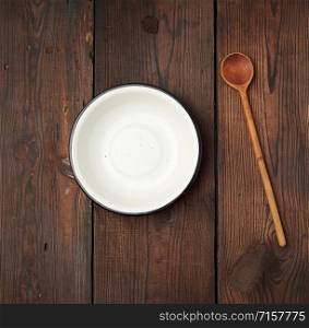 empty round metal white plate and wooden spoon on the table, top view