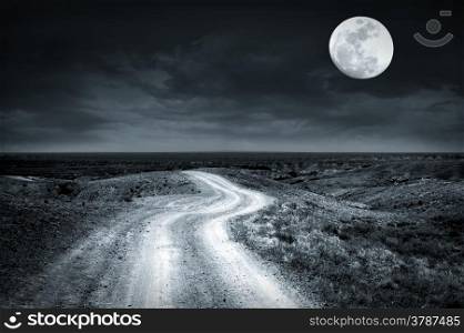 Empty rural road going through prairie at full moon night with dramatic cloudy sky