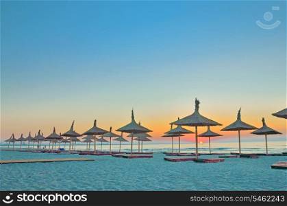 empty sandy beach with umbrellas and beach beds and sunrise