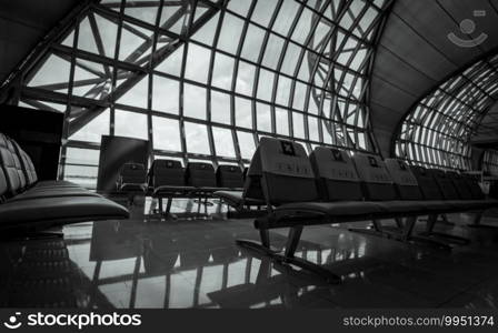 Empty seat in departure lounge at airport terminal. Social distancing for safety. Coronavirus crisis impact on aviation business. No passenger in the airport. Priority seating. Black and white scene.