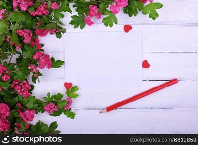 Empty sheet of paper and a red wooden pencil on a white surface, in the corner a branch of hawthorn with pink flowers