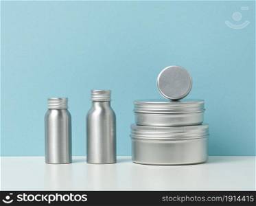 empty silver metal bottle for cosmetics on white table, blue background. Packaging for cream, gel, serum, advertising and product promotion. Mock up