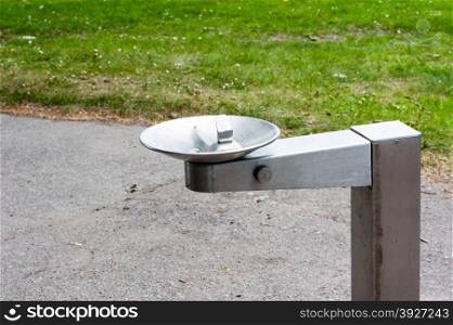 Empty silver metal water drinking fountain near park path and grass.