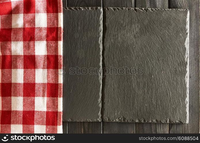 Empty slate plates and tablecloth over black wooden background