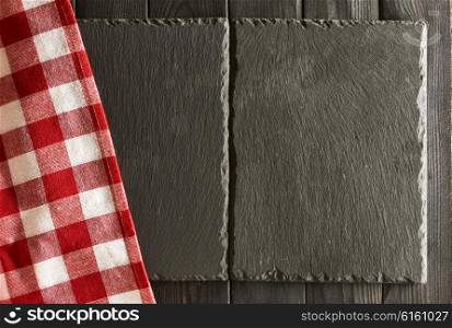 Empty slate plates and tablecloth over black wooden background