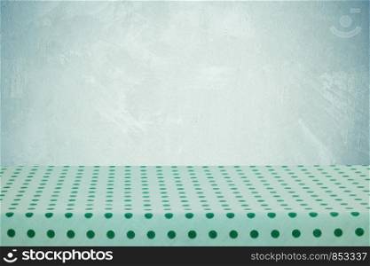 Empty table with green tablecloth over cement wall background, for food and product display montage