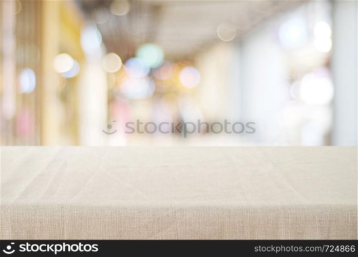 Empty table with linen tablecloth over blurred store with bokeh background, product display montage