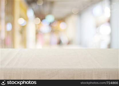 Empty table with linen tablecloth over blurred store with bokeh background, product display montage
