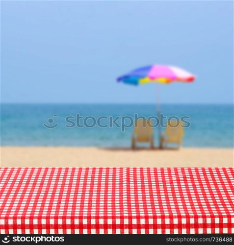 Empty table with red and white tablecloth over blurred sea outdoor nature background, for product display montage, spring and summer
