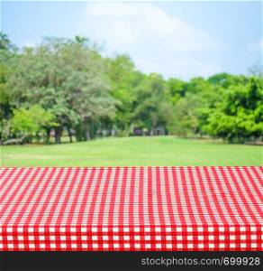 Empty table with red tablecloth over blur garden and bokeh background, for food and product display montage
