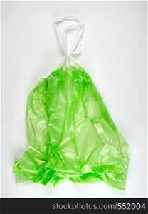 empty transparent green plastic garbage bag with handles on a white background