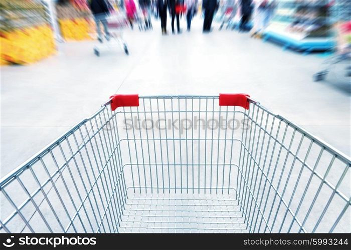 Empty trolley in supermarket or mall full of crowded people. Blur motion.