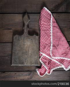 Empty very old kitchen cutting board with handle and red towel on a brown table, top view