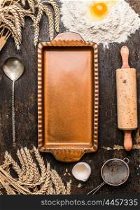 Empty vintage rustic tart mold with kitchen utensil for bake and ears on rustic wooden background, top view