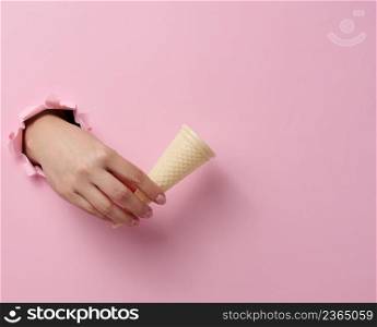 empty waffle cone ice cream cup in a woman&rsquo;s hand sticking out of a torn hole in a pink paper