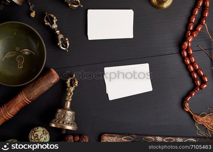 empty white business cards in the midst of Asian religious objects for meditation and alternative medicine on a black wooden background, top view