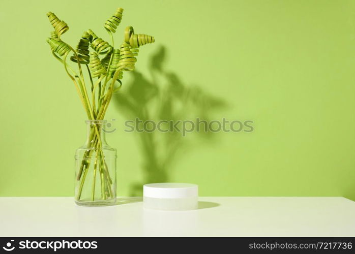 empty white jar for cosmetics on white table, green background. Packaging for cream, gel, serum, advertising and product promotion. Mock up