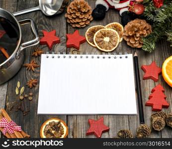 empty white paper notebook and black pencil and pan with mulled wine on a gray wooden background