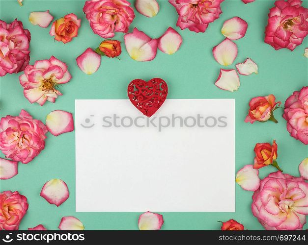 empty white paper sheet and red heart on a green background, on the perimeter of blooming pink roses, top view, copy space