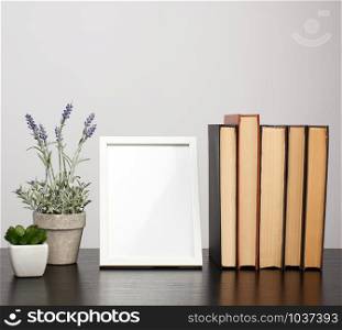 empty white photo frame, stack of books and a pot of growing lavender on a black table, workplace