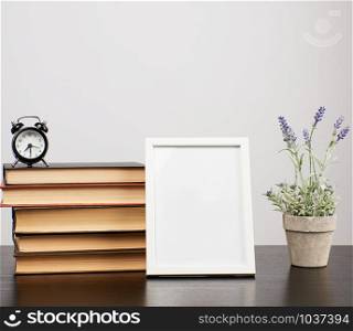 empty white photo frame, stack of books and a pot of growing lavender on a black table