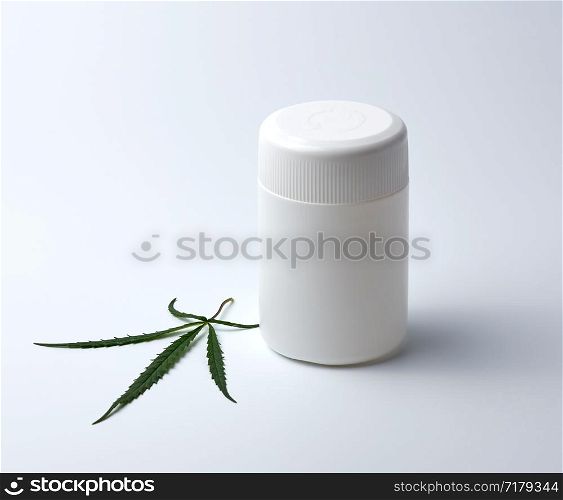 empty white plastic medical jar for pills and green hemp leaf on a white background, alternative medicine concept