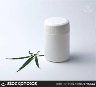 empty white plastic medical jar for pills and green hemp leaf on a white background, alternative medicine concept
