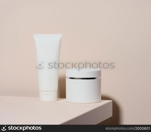 empty white plastic tube andjar for cosmetics stands on a beige background. Containers for cream, shampoos, liquid substances. Branding, template