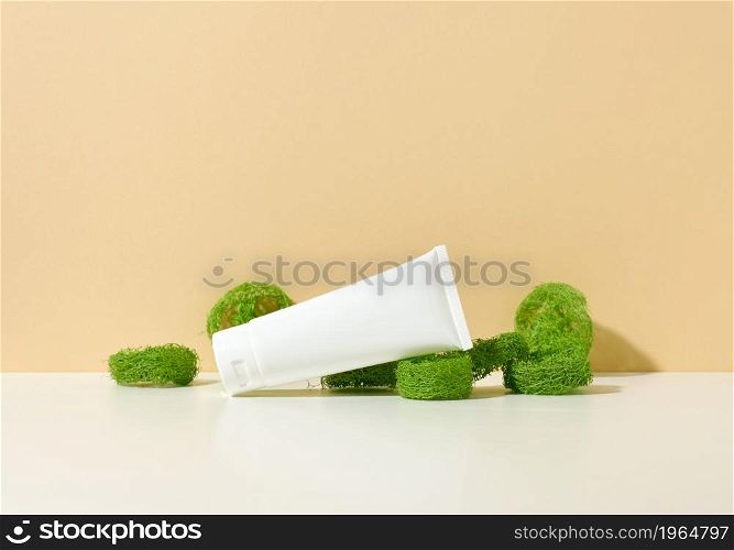 empty white plastic tube on a beige background and pieces of green loofah. Cosmetic products for branding gel, cream, lotion, shampoo. Mock up eco cosmetics