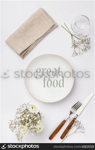Empty white plate and cutlery on a napkin, flat lay on white background