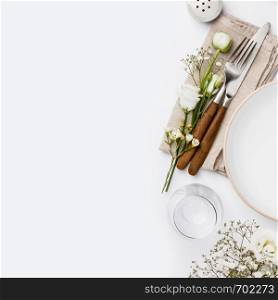 Empty white plate and cutlery on a napkin, flat lay on white background. Empty white plate and cutlery on a napkin