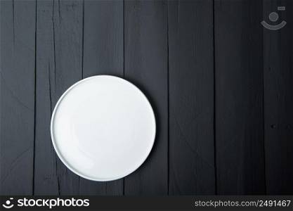 empty white plate on black wooden background. the food, the view from the top