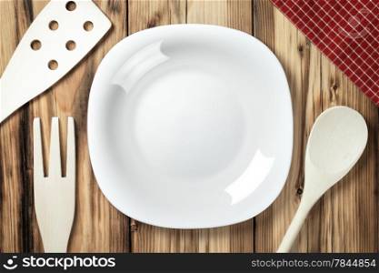 Empty white plate on table background with wooden cutlery and napkin. Top view