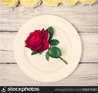 Empty white plate with a red rose on a white wooden background, vintage toning