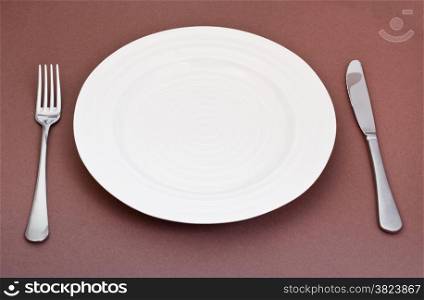 empty white plate with fork and knife set on brown background