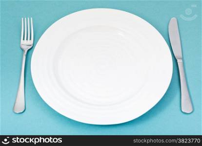 empty white plate with fork and knife set on green background