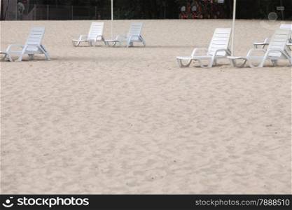 empty white pool plastic chairs deckchairs on sand beach. Vacation concept