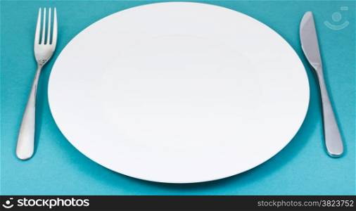 empty white porcelain plate with fork and knife set on green background