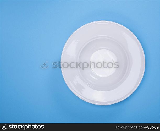 empty white round ceramic soup plate on a blue background, empty space on the left