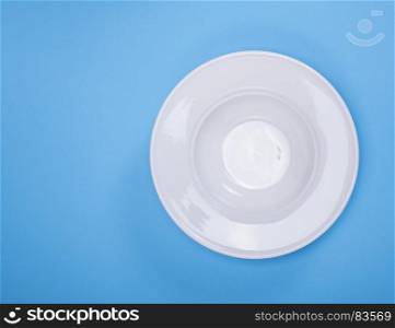 empty white round ceramic soup plate on a blue background, empty space on the left