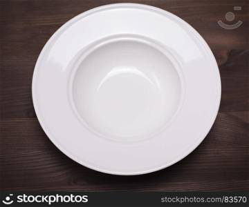 empty white round ceramic soup plate on a brown wooden background