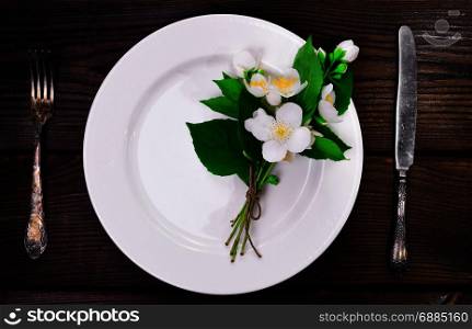 empty white round plate with iron vintage cutlery on a brown wooden background, top view