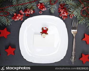 empty white square plate, fork and christmas decor on a black background, top view
