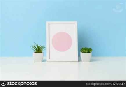 empty white wooden photo frame and flowerpots with plants on white table, blue background